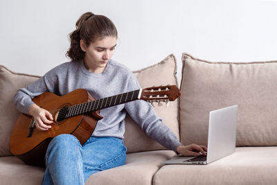 Girl using laptop while playing guitar