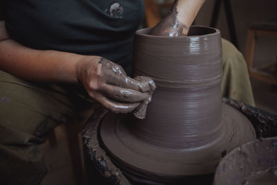 A middle-aged woman works on a potter's wheel, her face is not visible