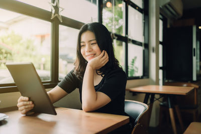 Portrait of young woman using phone while sitting on table