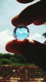 Close-up of hand holding leaf against sky
