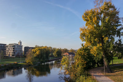 Scenic view of river by trees and buildings against sky