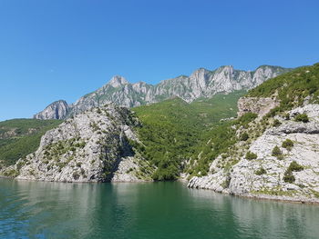 Scenic view of lake and mountains against clear blue sky