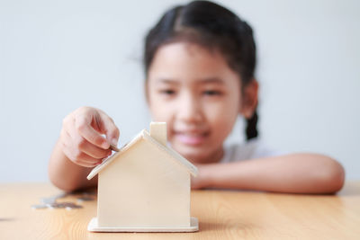 Close-up of smiling girl with coins and model home on table