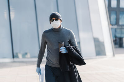 Man wearing mask holding coffee cup and newspaper in city