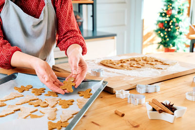 Woman's hands putting cookies a shape of christmas gingerbread on oven paper.