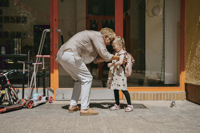 Senior woman tickling granddaughter while standing near door of kindergarten