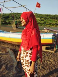 Side view of smiling girl wearing headscarf while standing at beach