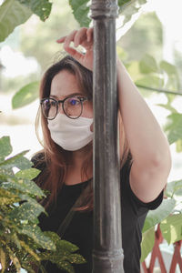 Woman wearing mask standing by pol