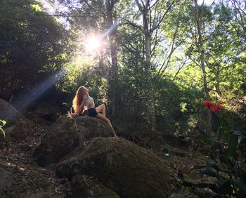 Low angle view of young woman sitting on rock at forest