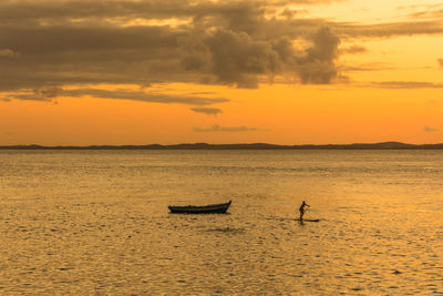 Woman paddleboarding on sea against sky during sunset