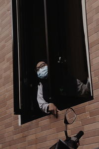 Portrait of young woman wearing mask standing at window