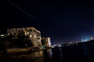 Illuminated buildings by river against sky at night