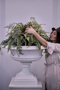 Woman holding plant in urn while standing against wall