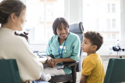 Smiling pediatrician sitting while son looking at mother in hospital