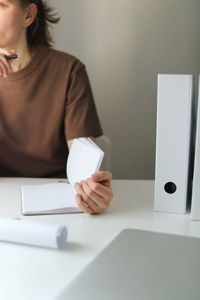 Midsection of woman holding paper while sitting on table