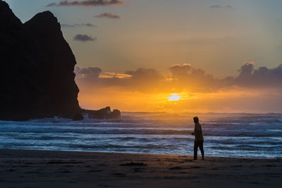 Silhouette man standing on beach against sky during sunset