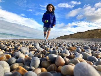 Full length of boy standing on pebbles at beach