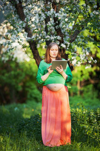 Pregnant woman using digital tablet while standing on grass