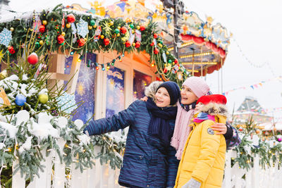 Smiling mother and kids standing against christmas decoration outdoors