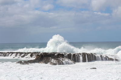 Waves splashing on shore against sky
