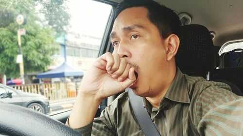 Tired man yawning while driving car