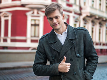 Portrait of businessman showing thumbs up while standing on city street