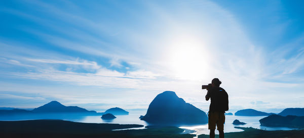 Rear view of man with arms raised against sky during sunset