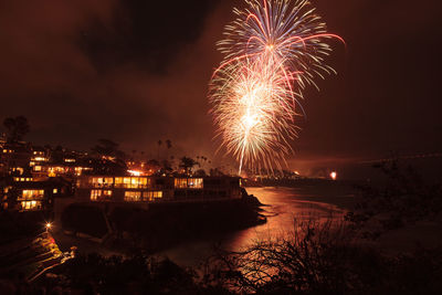 Illuminated fireworks over beach against sky in city at night