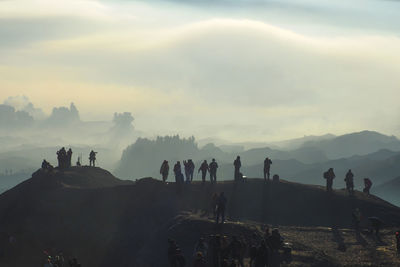 Silhouette people standing on mountain peak during foggy weather