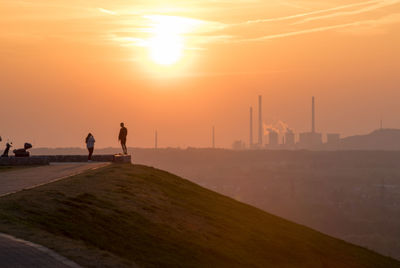 Silhouette people standing on land against sky during sunset