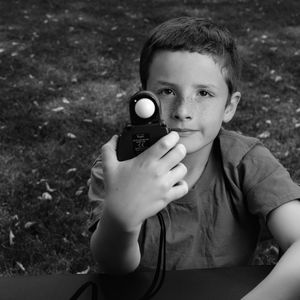 Portrait of boy holding camera on field