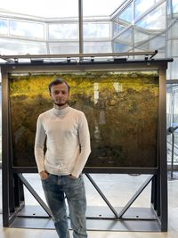 Portrait of young man standing against window