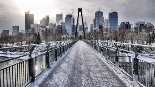 Bridge amidst buildings in city against sky during winter