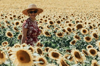 Woman in straw hat and red dress standing in yellow sunflower field and smiling at camera