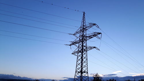 Low angle view of electricity pylon against clear blue sky