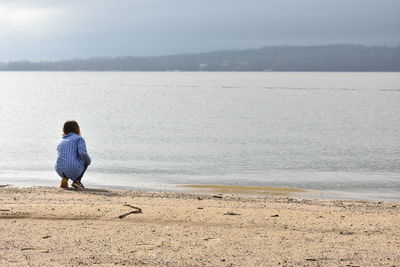 Rear view of boy on beach against sky