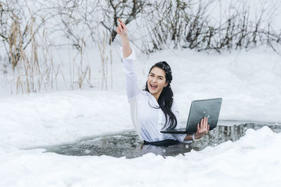 Full length of young woman sitting on snow covered field