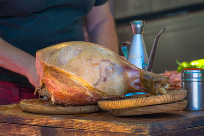 Midsection of person with ham at table in kitchen