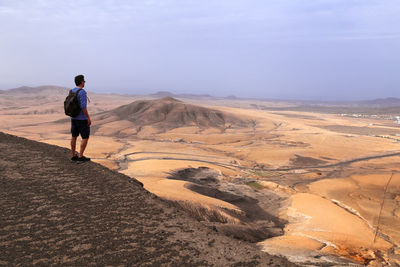 Rear view of man standing at the top of the hill watchong desert volcanic landscape, fuerteventura