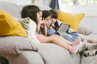Children using digital tablet on sofa in living room at home