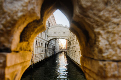 Bridge over canal seen through arch amidst old buildings