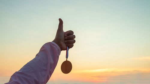 Midsection of man holding umbrella against sky during sunset