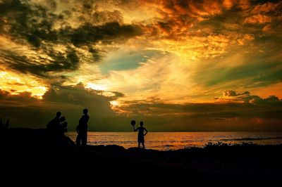 Silhouette people on beach against sky during sunset