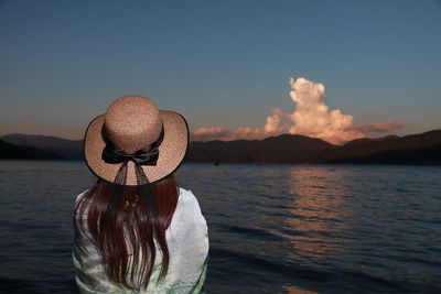 Rear view of woman in hat by lake against sky