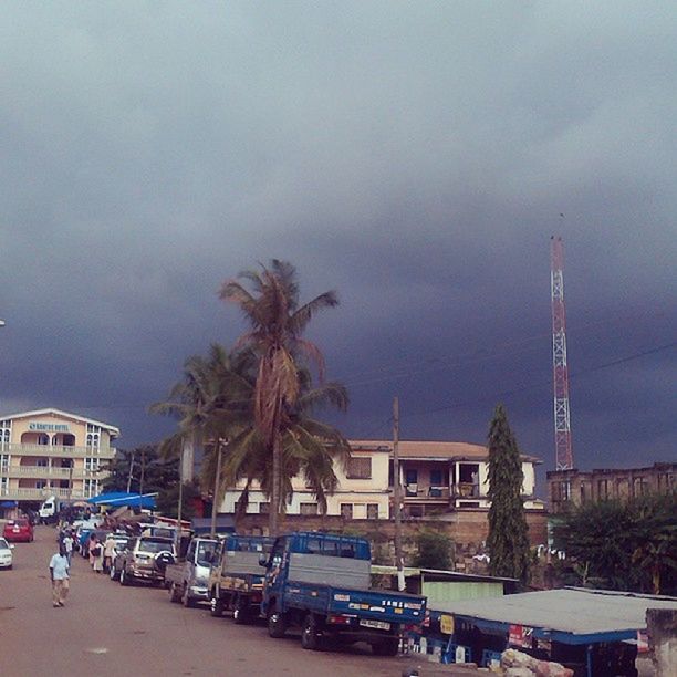 building exterior, architecture, built structure, transportation, sky, car, mode of transport, land vehicle, city, street, road, cloud - sky, palm tree, tree, cloudy, weather, incidental people, street light, city life, overcast