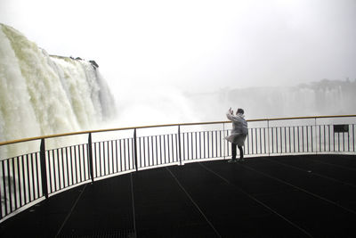 Tourist photographing waterfall by railing