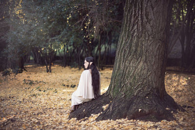 Fairy elf young woman sitting by tree during autumn