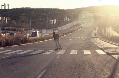 Skateboarder on empty road against clear sky on sunny day