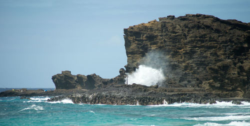 Sea waves splashing on rock formation against sky
