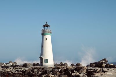 Lighthouse on rock by building against sky